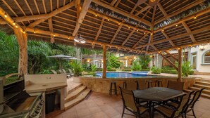 An outdoor patio with a grill, dining table, and pool. - Harmon House (Jacó)