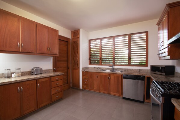 Una cocina con armarios de madera, lavavajillas de acero inoxidable, microondas y estufa.