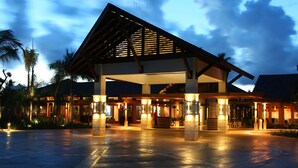 A modern hotel entrance with a covered walkway, palm trees, and a wet pavement. - Claro de Luna by Casa de Campo Resort & Villas (La Romana)