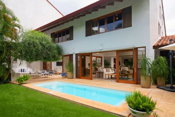 Ein zweistöckiges Haus mit Swimmingpool, Sitzgelegenheit im Freien und Topfpflanzen.