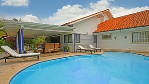 A swimming pool with lounge chairs, a covered patio, and a house with a red-tiled roof. - Casa del Rocio by Casa de Campo Resort & Villas (La Romana)