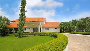 A two-story house with a red-tiled roof, surrounded by well-maintained greenery and a paved driveway. - Casa del Rocio by Casa de Campo Resort & Villas (La Romana)