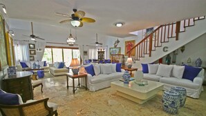 A spacious living room with white sofas, blue cushions, and decorative vases. A wooden staircase with a railing leads to another level. - Casa del Rocio by Casa de Campo Resort & Villas (La Romana)