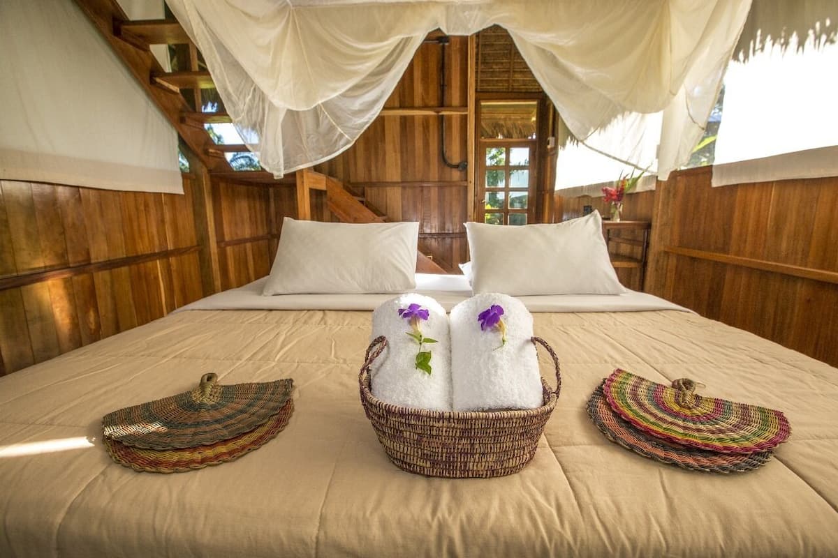 Een houten kamer met een bed, twee manden handdoeken en een hemelbed.