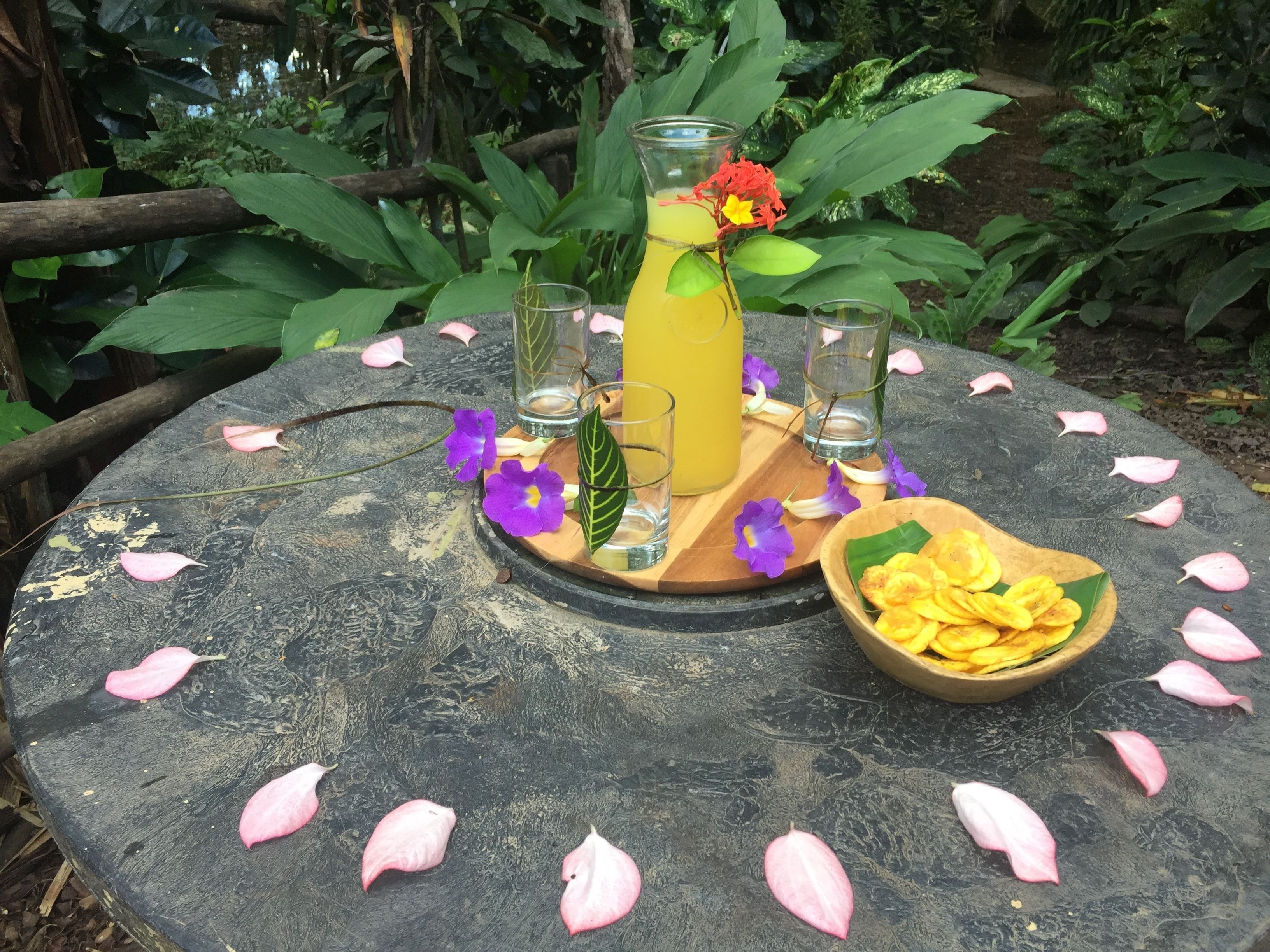 Une table ronde avec un pichet en verre, deux verres, un bol de fruits secs et des pétales de fleurs éparpillés.