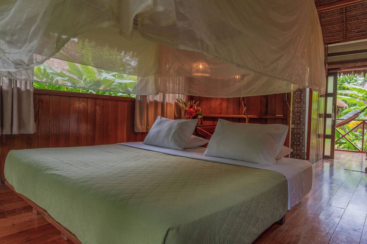 Een bed met hemelbed, houten wanden en uitzicht op groen.
