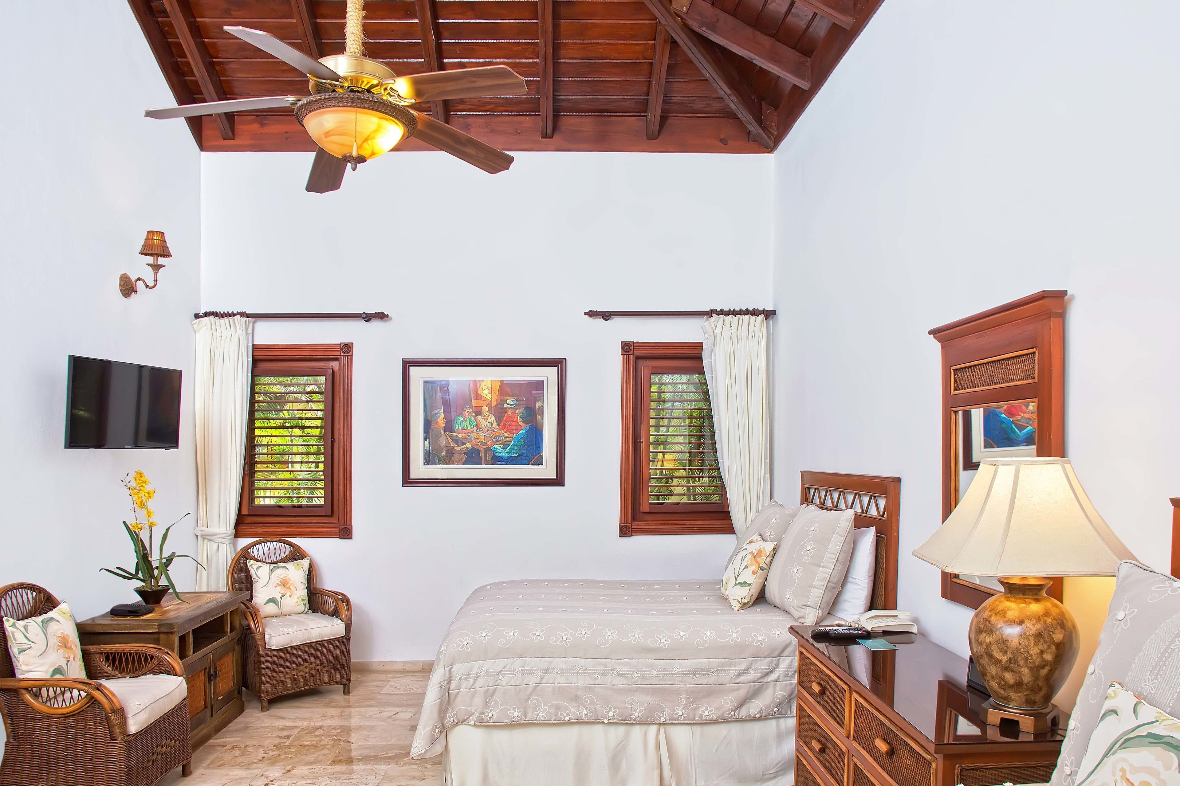 A bedroom with a bed, two chairs, a table, a lamp, a TV, and artwork on the walls.