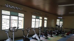 A gym with stationary bikes and treadmills, large windows with a stone wall view, and colorful mats on the floor. - Akagera Resort and Country Club (Rwimbogo)