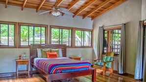Une chambre à coucher avec un lit en bois, une table de chevet, une chaise et de grandes fenêtres donnant sur un paysage verdoyant.