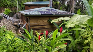 Une cabane en bois, dotée d’un toit en pente, entourée d’une végétation luxuriante et accessible par un petit escalier menant à l’entrée.