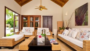 A spacious living area with wicker furniture, a ceiling fan, and a large window offering a view of greenery.