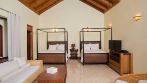 A room with two four-poster beds, a sofa, a TV stand, and a small table.