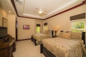 Two single beds with matching headboards and footboards, a ceiling fan, TV, and framed picture adorn this cozy space.