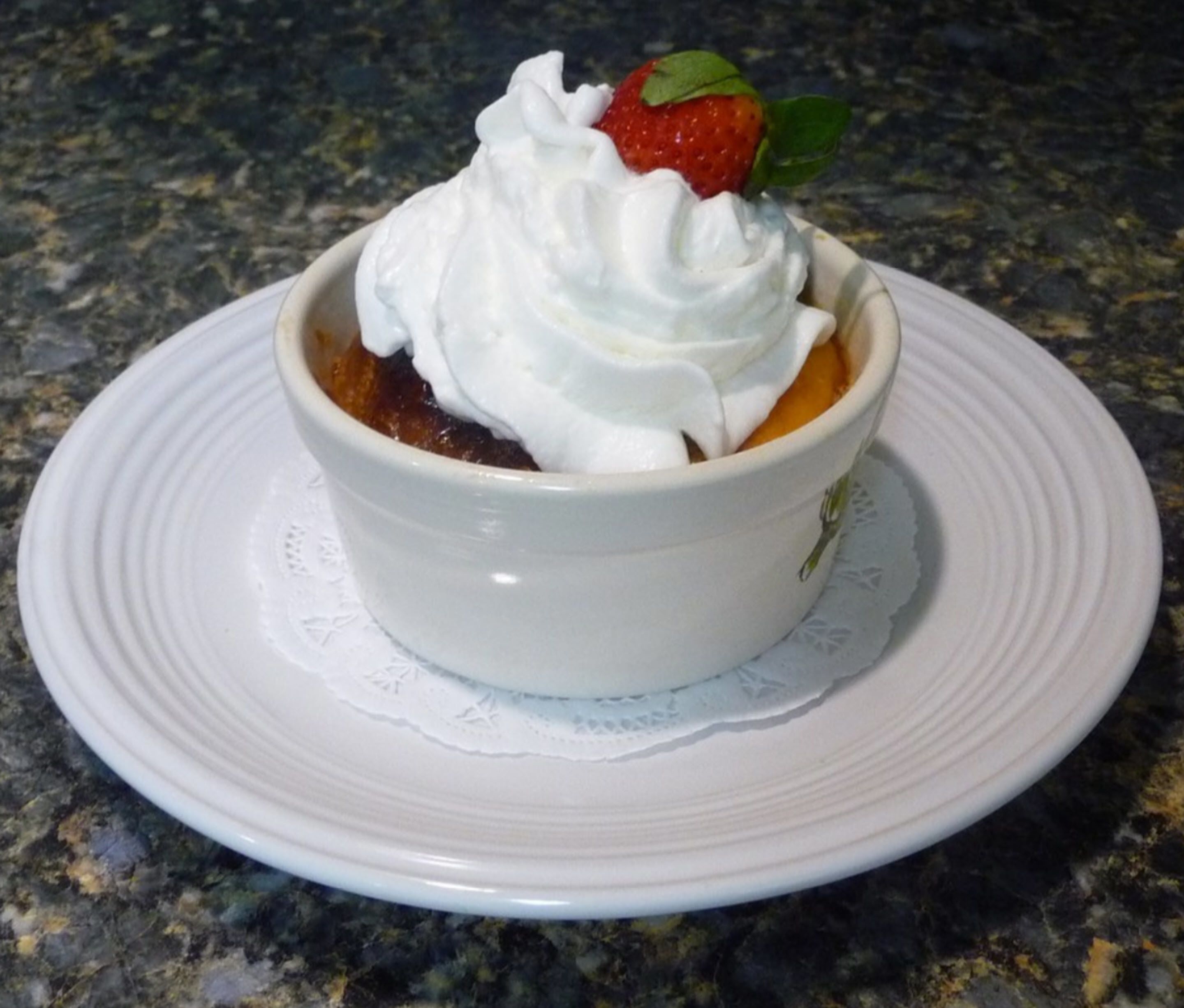 Un postre en un tazón blanco sobre un plato blanco con un encaje debajo.