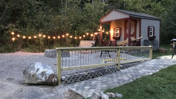 A small wooden cabin with a porch, surrounded by a gravel path and string lights. - Seams Like Home B&B (Connellsville)