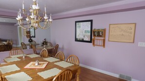 A dining room with a large wooden table, six chairs, a chandelier, and framed artwork on the walls. - Seams Like Home B&B (Connellsville)