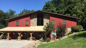 A two-story house with a red exterior and stone accents, featuring a front porch with potted plants and a gravel driveway. - Seams Like Home B&B (Connellsville)