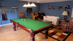 A pool table in a room with a blue wall, a white sofa, and a plaid chair. - Seams Like Home B&B (Connellsville)