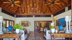 A spacious lobby with wooden furniture, a chandelier, ceiling fans, and potted plants.