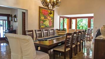 A dining area with a large wooden table, multiple chairs, a chandelier, and a colorful painting on the wall.