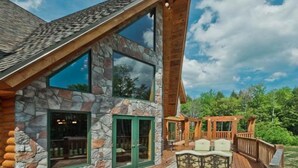 A log cabin with large windows, a stone facade, and a wooden deck with outdoor seating.