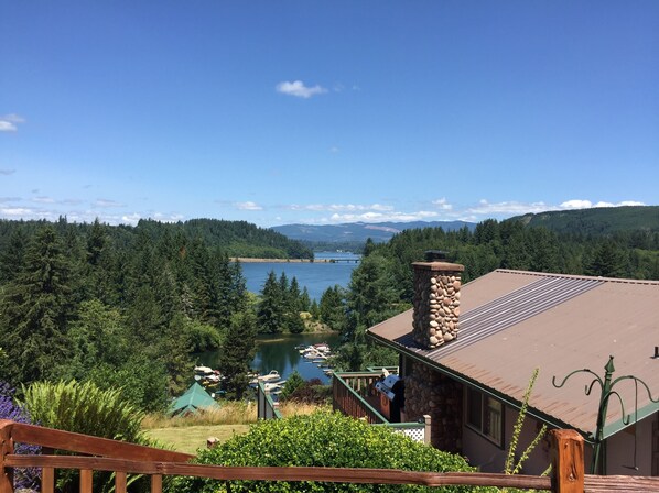 A lakeside cabin with a stone chimney, a deck overlooking the water, and a view of the surrounding forest and mountains. - Spectacular lake view! (Mossyrock)