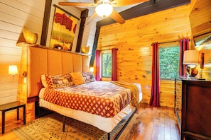 Un dormitorio tipo cabaña de madera con una cama, mesitas de noche, un aparador y un ventilador de techo.