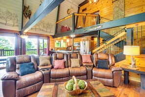 Interior acogedor de una cabaña con un sofá seccional de cuero, una mesa de comedor y una escalera que sube a un nivel superior.
