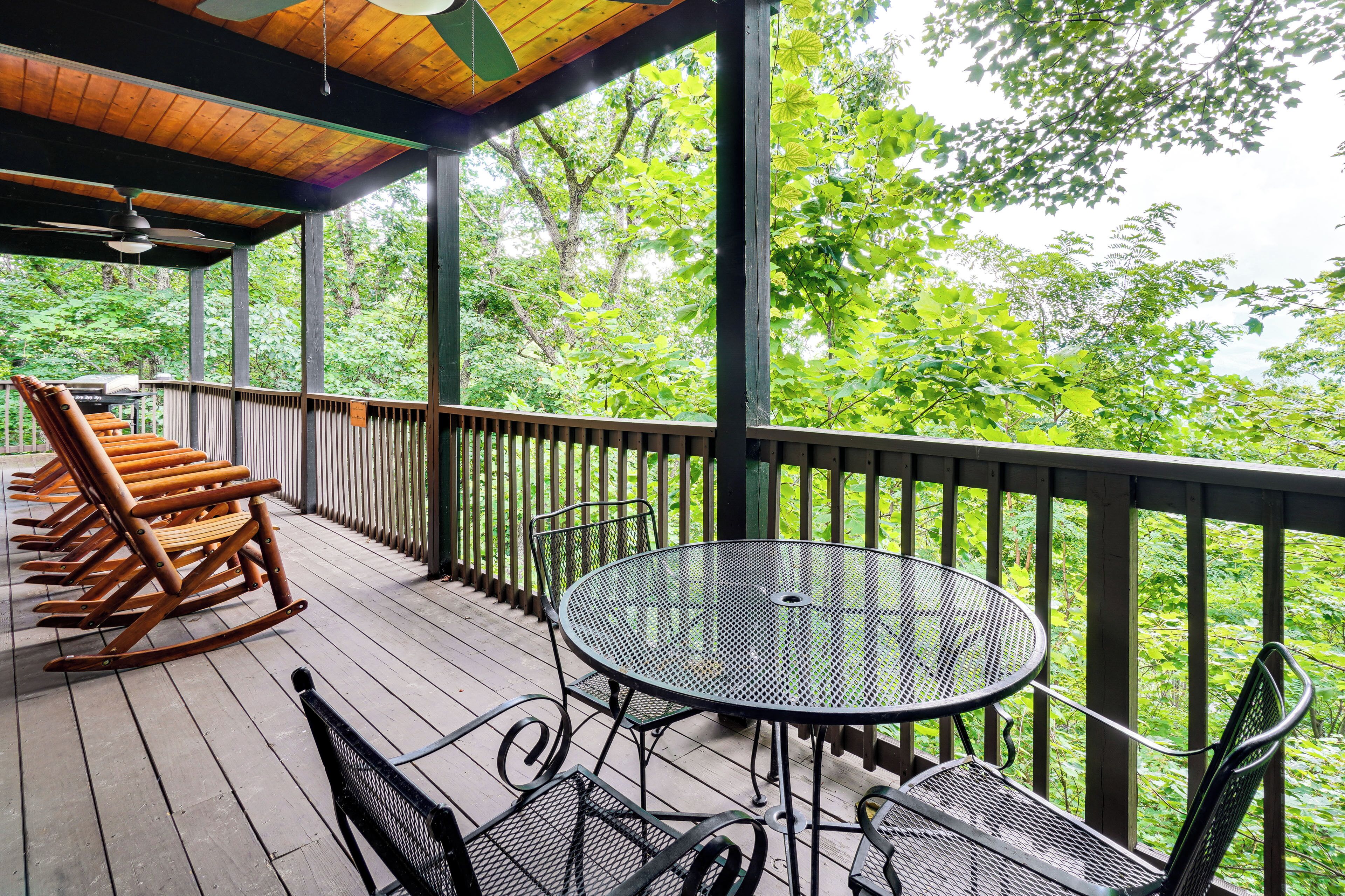 Une terrasse en bois avec des fauteuils à bascule et une table ronde entourée de chaises.