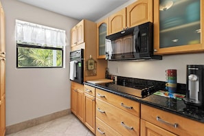 A kitchen with wooden cabinets, a black microwave, and a stainless steel refrigerator.