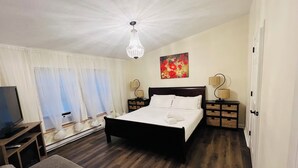 A bedroom with a large bed, a TV, a sofa, and a chandelier. - Tranquilla Villa. Bi Level Deck, HOT TUB, fire pit, grill, Movie & Game Rooms! (Tobyhanna)