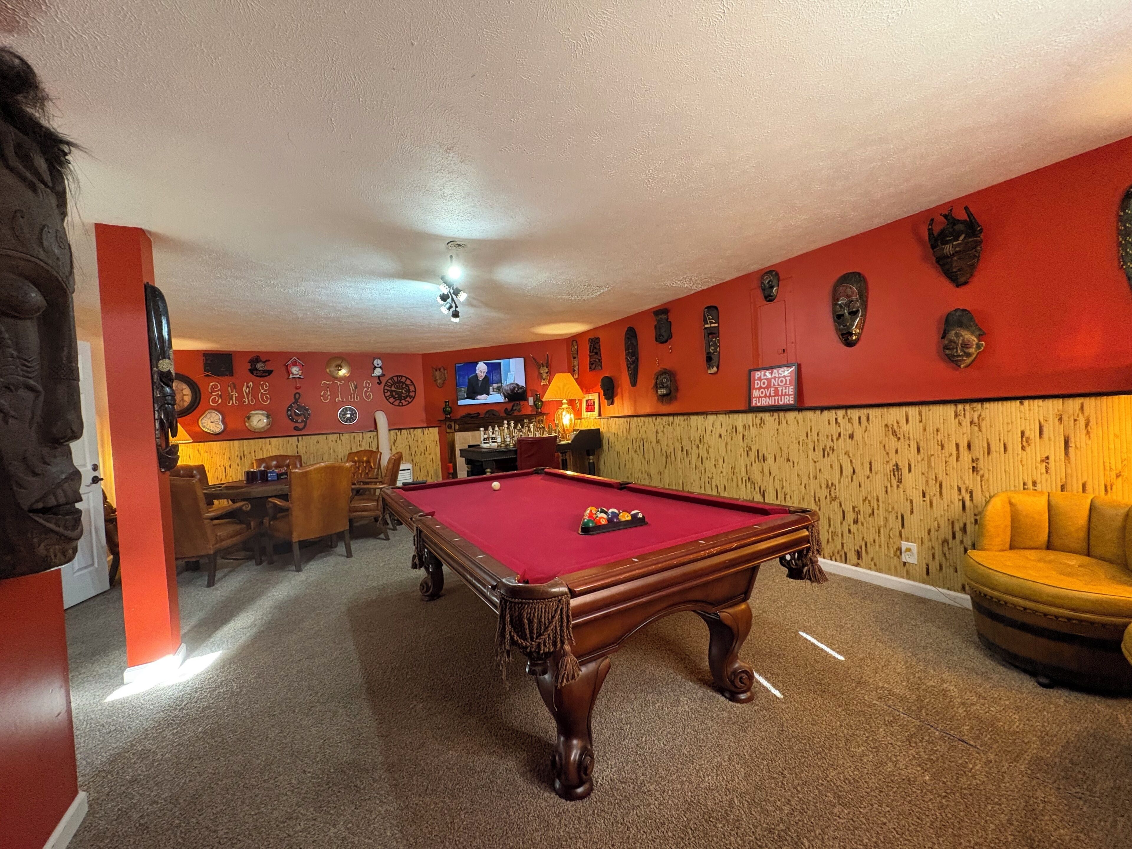 Una mesa de billar en una habitación con paredes rojas, un televisor y varias decoraciones en las paredes.