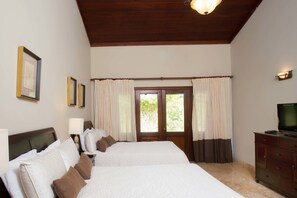 A hotel room with two beds, a wooden ceiling, a television on a dresser, and a window with curtains.