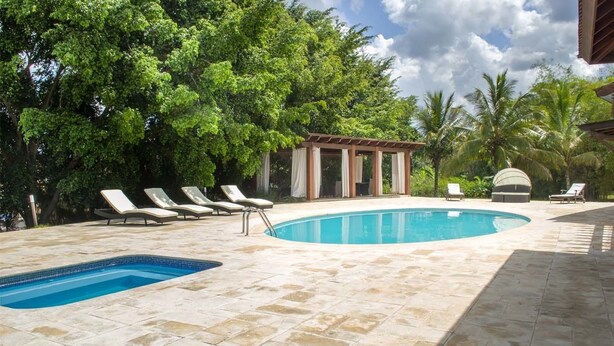 Piscina com espreguiçadeiras e um gazebo rodeado por vegetação exuberante.