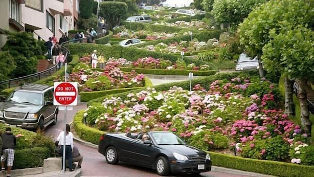 Ein Garten mit einem 'DO NOT ENTER'-Schild, einem schwarzen Auto und einem Gebäude mit Personen auf der Treppe.