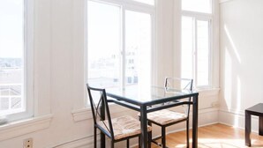 Ein Zimmer mit Glastisch und Stühlen, großen Fenstern und Blick auf Gebäude.