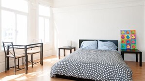 Ein Schlafzimmer mit einem Bett, einem Sessel, einem Tisch und einem farbenfrohen Kunstwerk an der Wand.