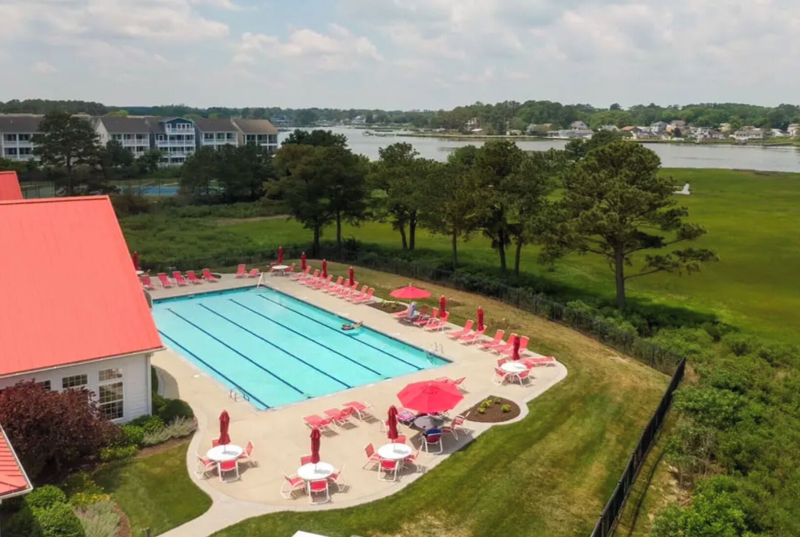 A swimming pool with lounge chairs and umbrellas, surrounded by greenery and a view of a lake.