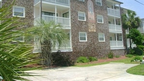A multi-story building with balconies, a stone facade, and a small garden area.