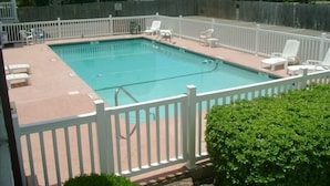 A rectangular swimming pool with a white fence and lounge chairs.