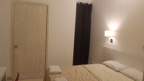 Een hotelkamer met een bed, een deur, een gordijn en een wandlamp.