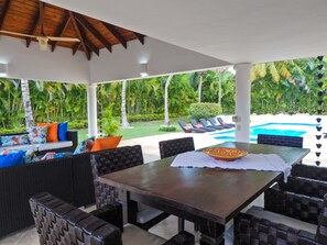 An outdoor dining area with a pool view, covered patio, and lush greenery. - Villa Toscano by Casa de Campo Resort & Villas (La Romana)