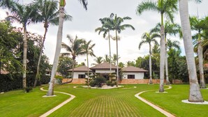 A well-maintained garden with a central lawn, palm trees, and a building with a tiled roof. - Villa Toscano by Casa de Campo Resort & Villas (La Romana)