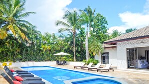 A swimming pool with lounge chairs and a table, surrounded by palm trees and a building with large windows. - Villa Toscano by Casa de Campo Resort & Villas (La Romana)