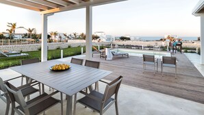 Eine überdachte Terrasse im Freien mit Pool, Essbereich und Blick auf Strand und Meer.