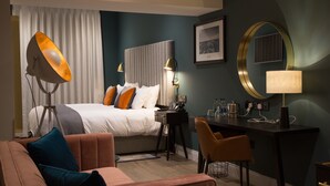 Una habitación de hotel con cama, escritorio, silla, lámpara y espejo.