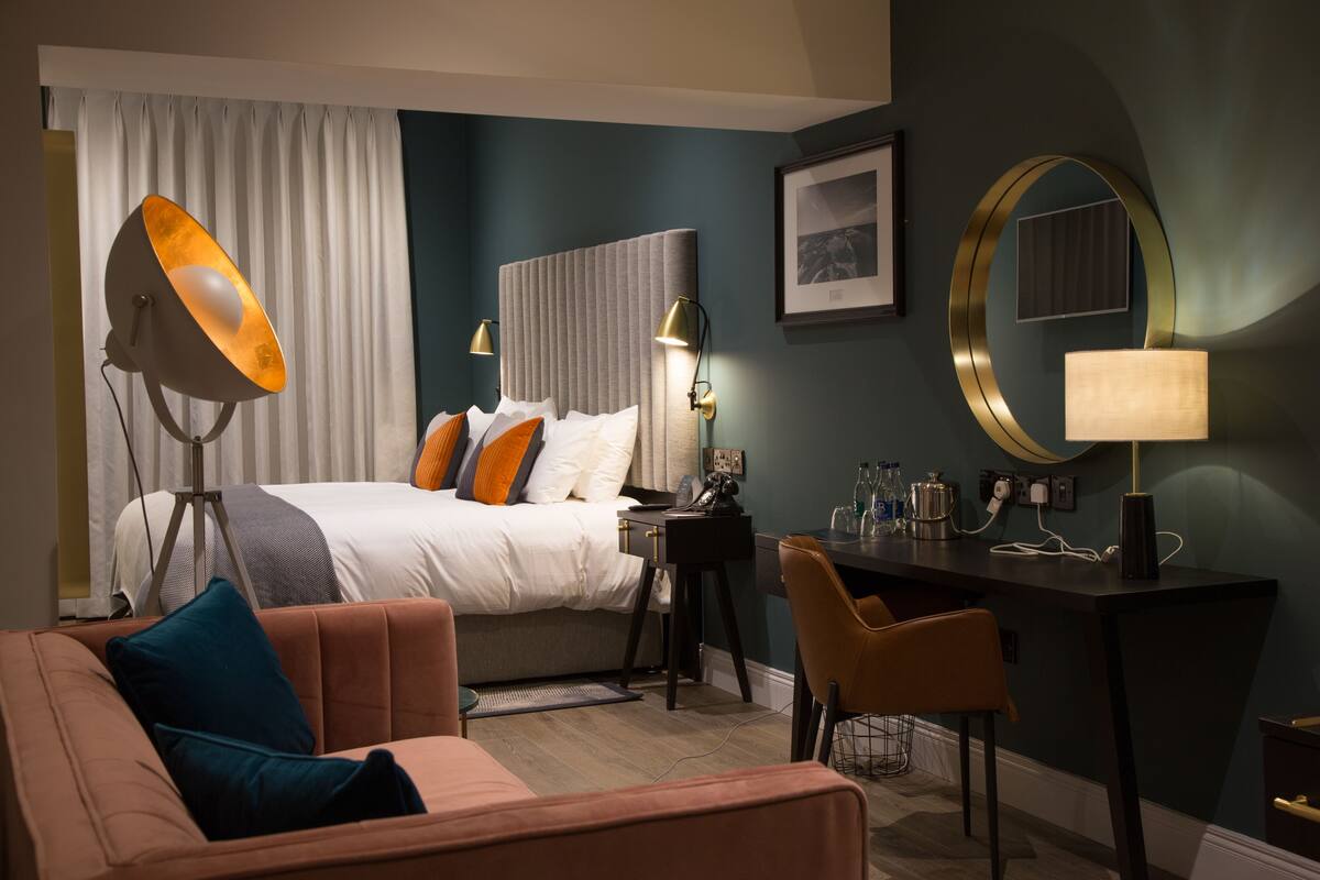 Una habitación de hotel con cama, escritorio, silla, lámpara y espejo.
