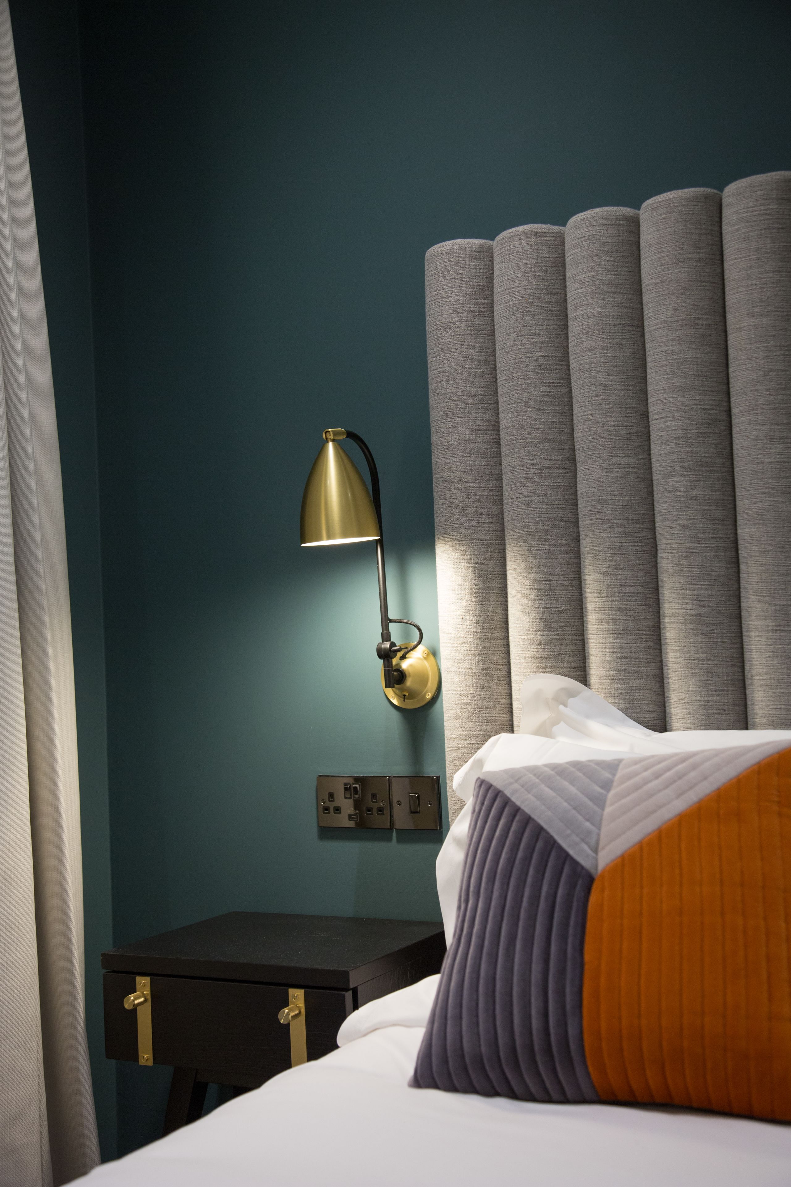 A neatly made bed with a striped pillow, a bedside lamp, and a power outlet on a wall.