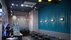 Interior moderno de una cafetería con barra, asientos y un menú en la pizarra.