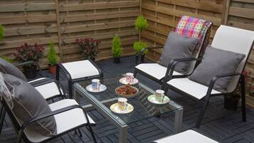 A patio area with a glass table, four chairs, and a small table with cups and a bowl.